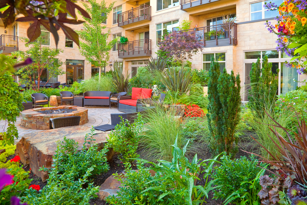Inviting courtyard garden at the Aljoya Mercer Island, independent living and assisted living, retirement community, featuring lush landscaping, comfortable seating, water feature, and fire pit for seniors to relax and socialize outdoors in Mercer Island.