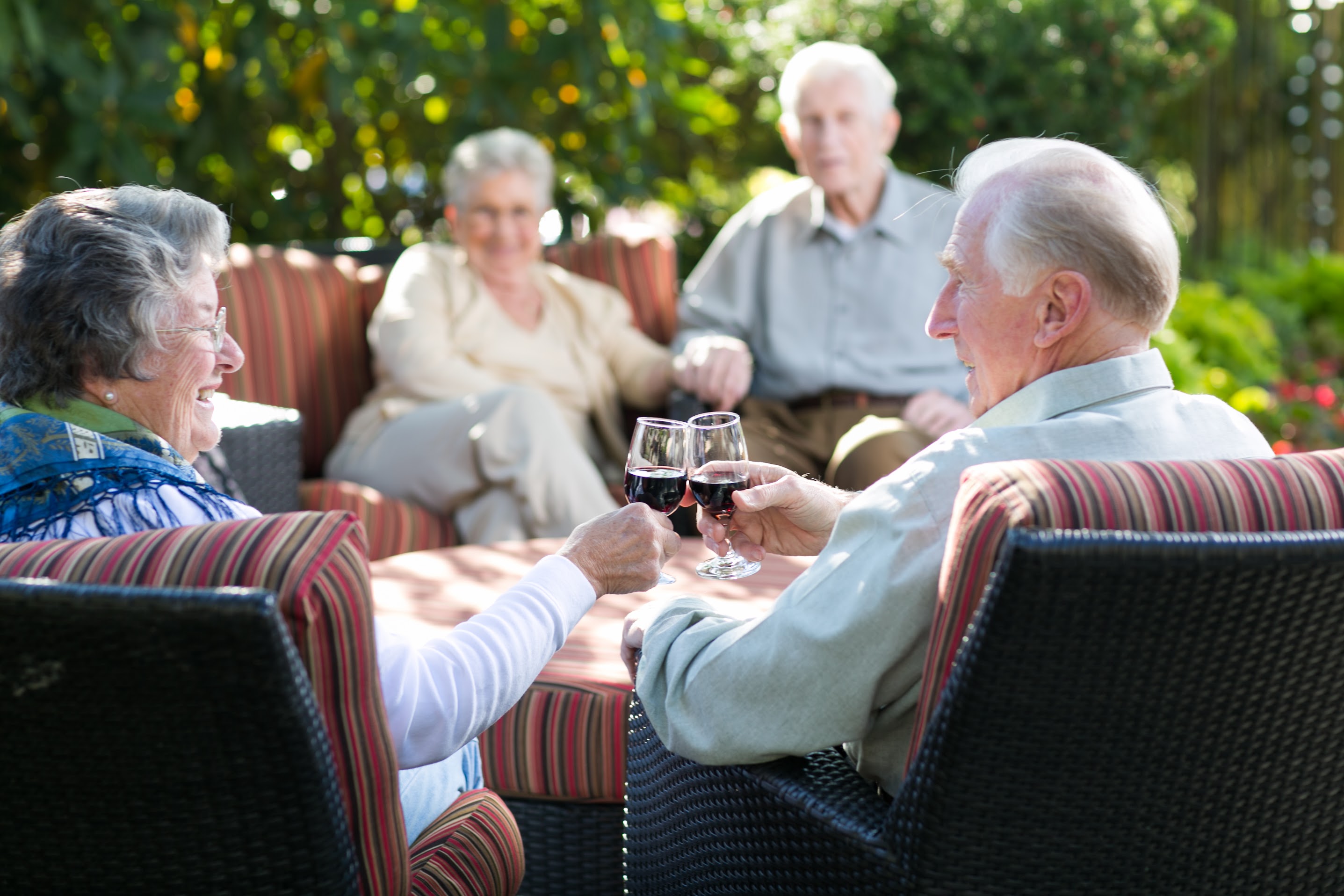 Older couple enjoying time outside in the garden with friends drinking wine.