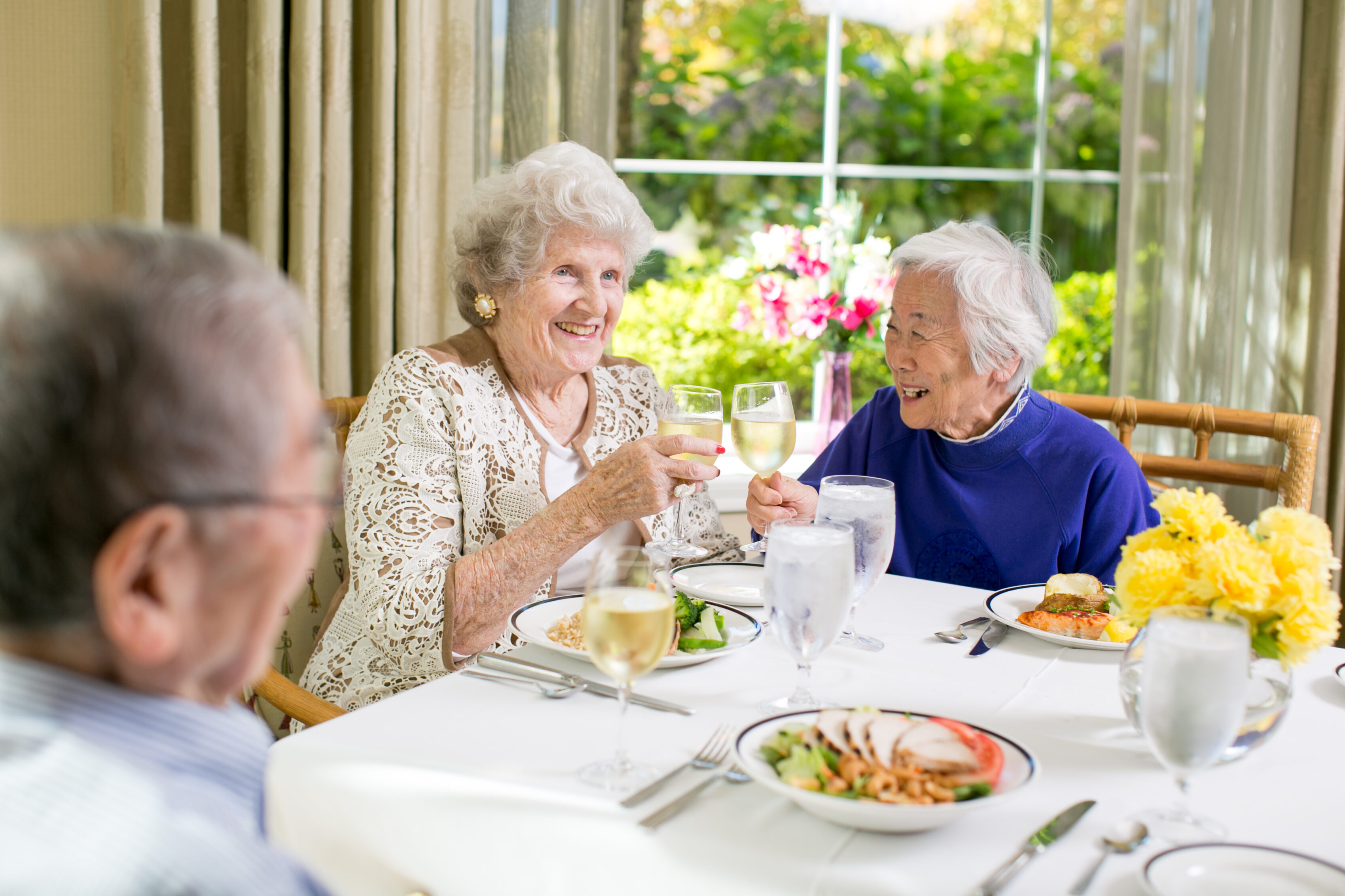 three older adults dining together and cheering at University House Issaquah senior living retirement community.