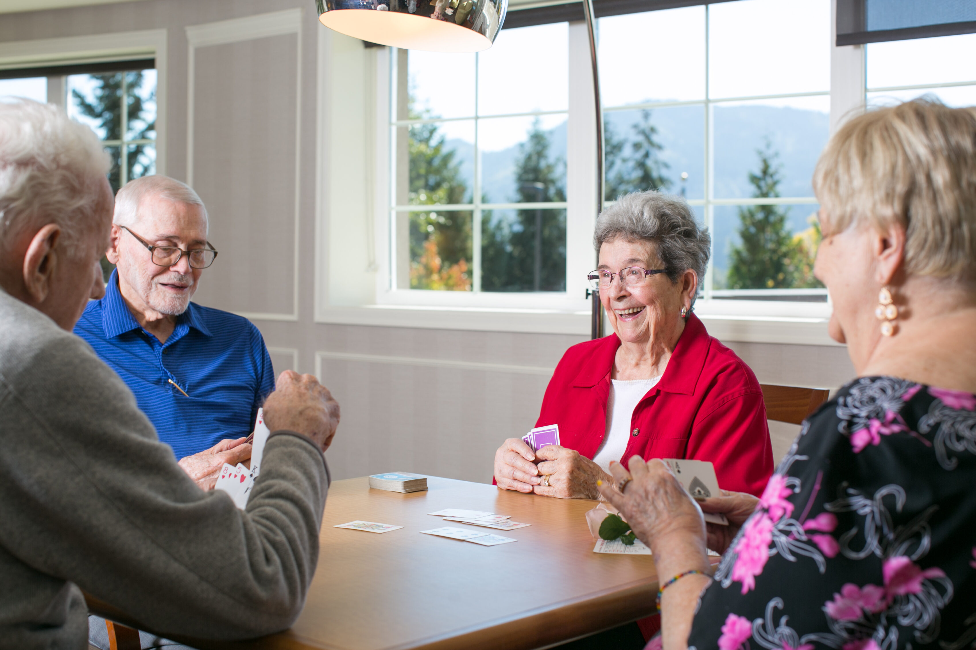 Friends laughing and playing cards with a view of the mountains out the window.