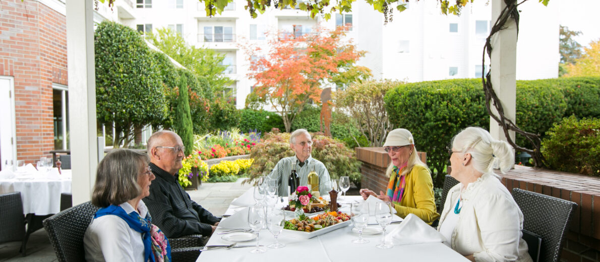 Friendly neighbors in a group setting enjoying lunch outside in courtyard of Seattle retirement community