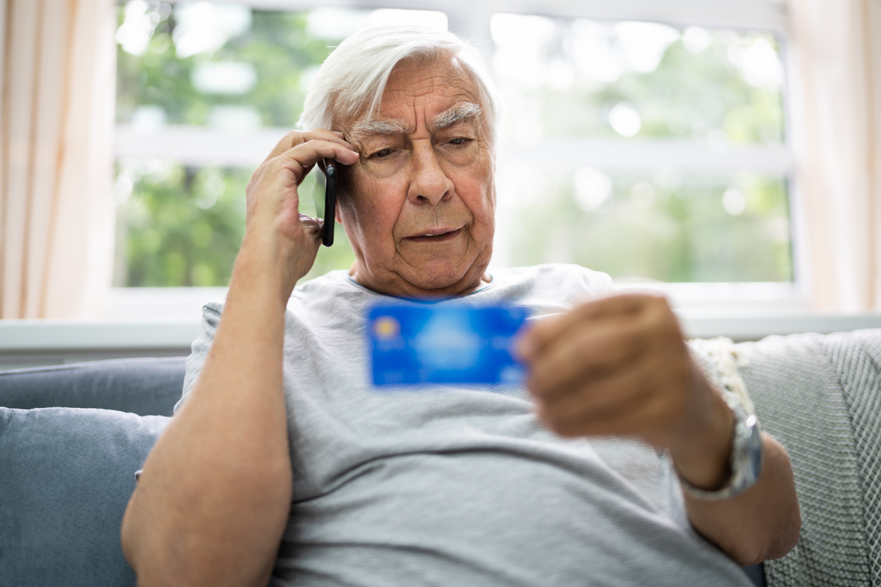 An older man on his cell phone looking at his credit card.