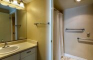 Apartment bathroom with safety grab-bars, shower, and vanity with sink, decorative lighting and cabinets.