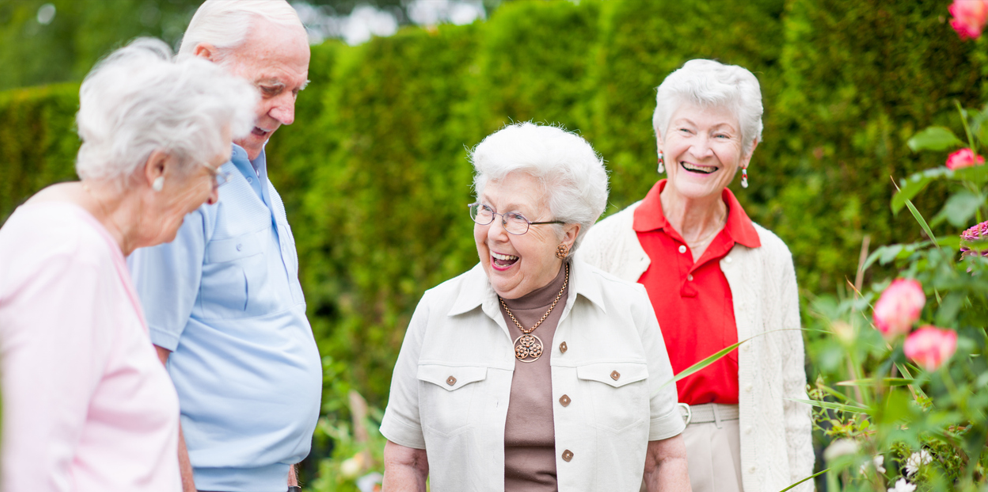 Group of four smiling older aduts walking outside in a garden