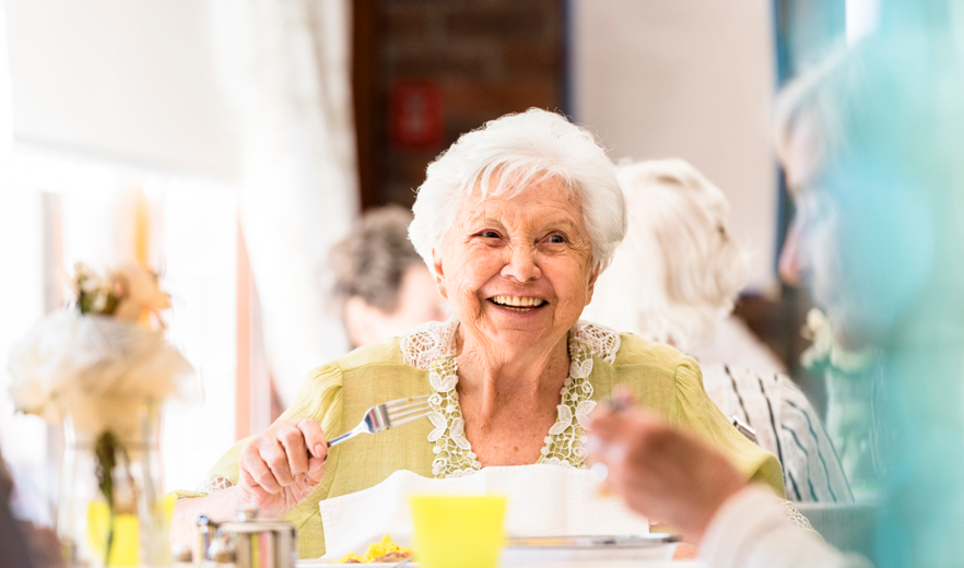Smiling older woman sitting at a table eating.