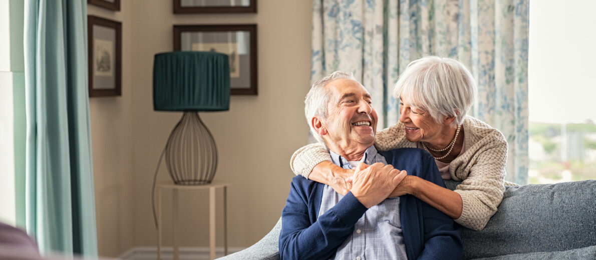 Happy senior woman embracing her husband at home while laughing together.