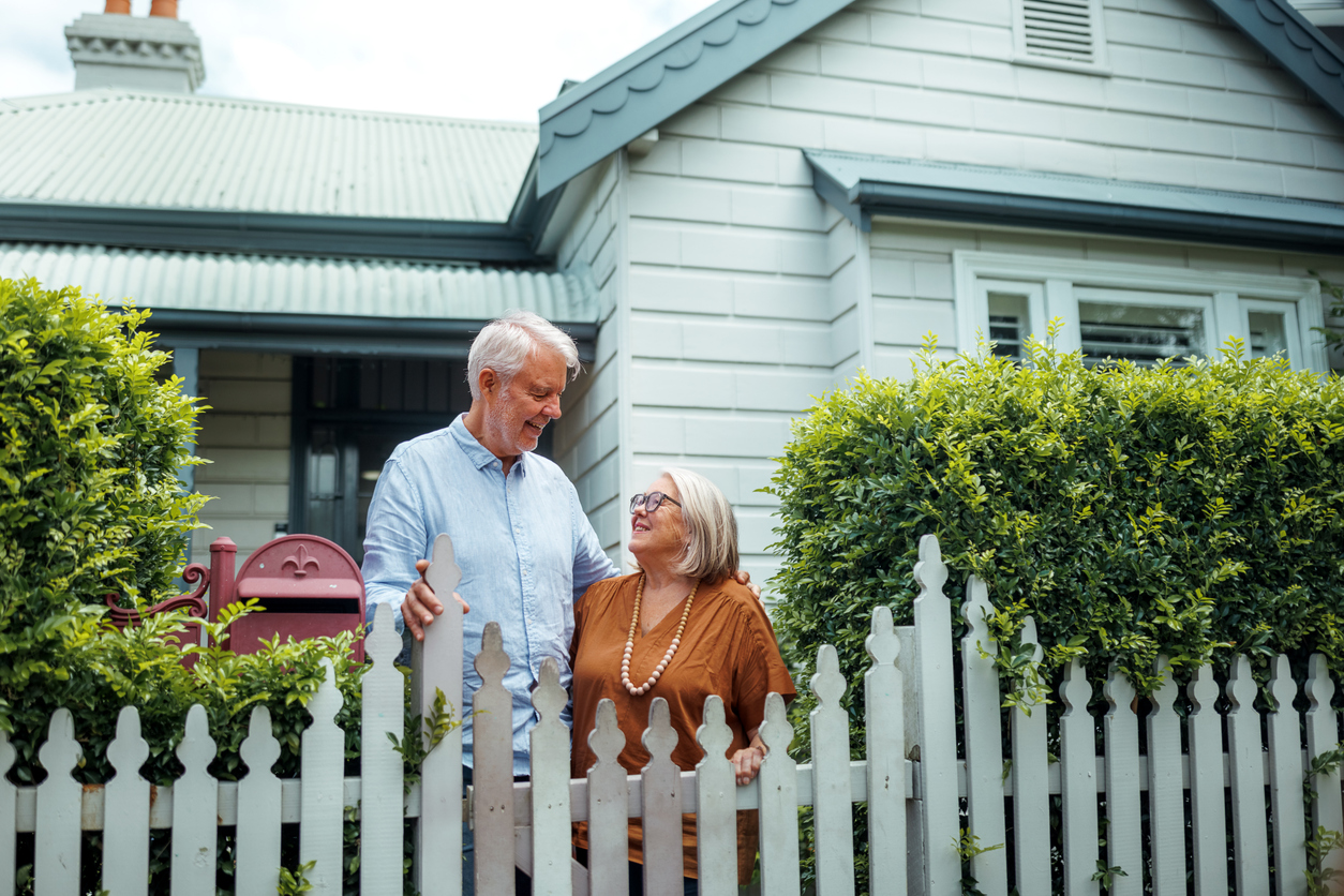Smiling older couple standing in front of their home.